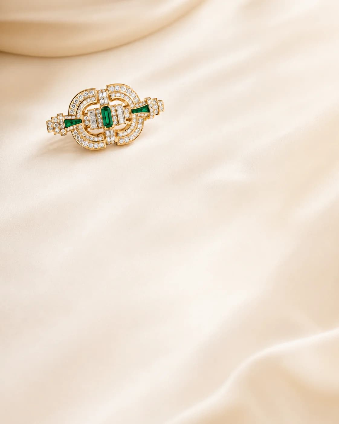 Gold and emerald jewellery on a warm ivory editorial background